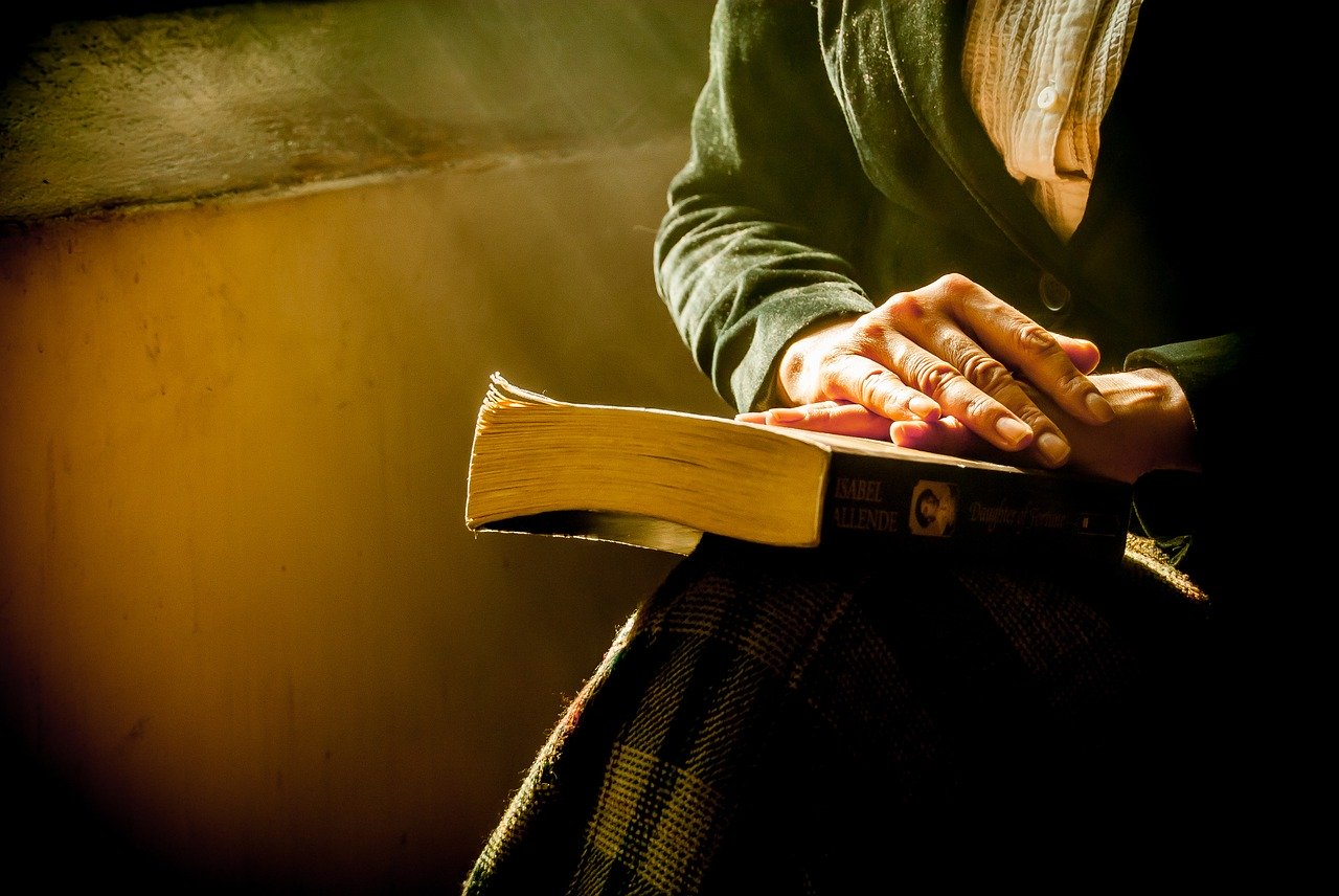 Das Bild zeigt eine alte Frau mit einem Buch auf dem Schoß