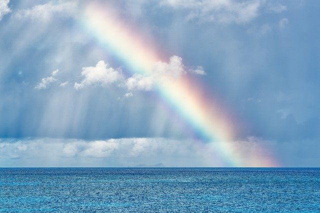 Das Bild zeigt einen Regenbogen über dem Meer mit wolkigem Himmel