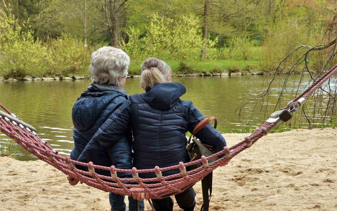 zwei Frauen sitzen auf einer Hängematte und blicken auf einen Teich